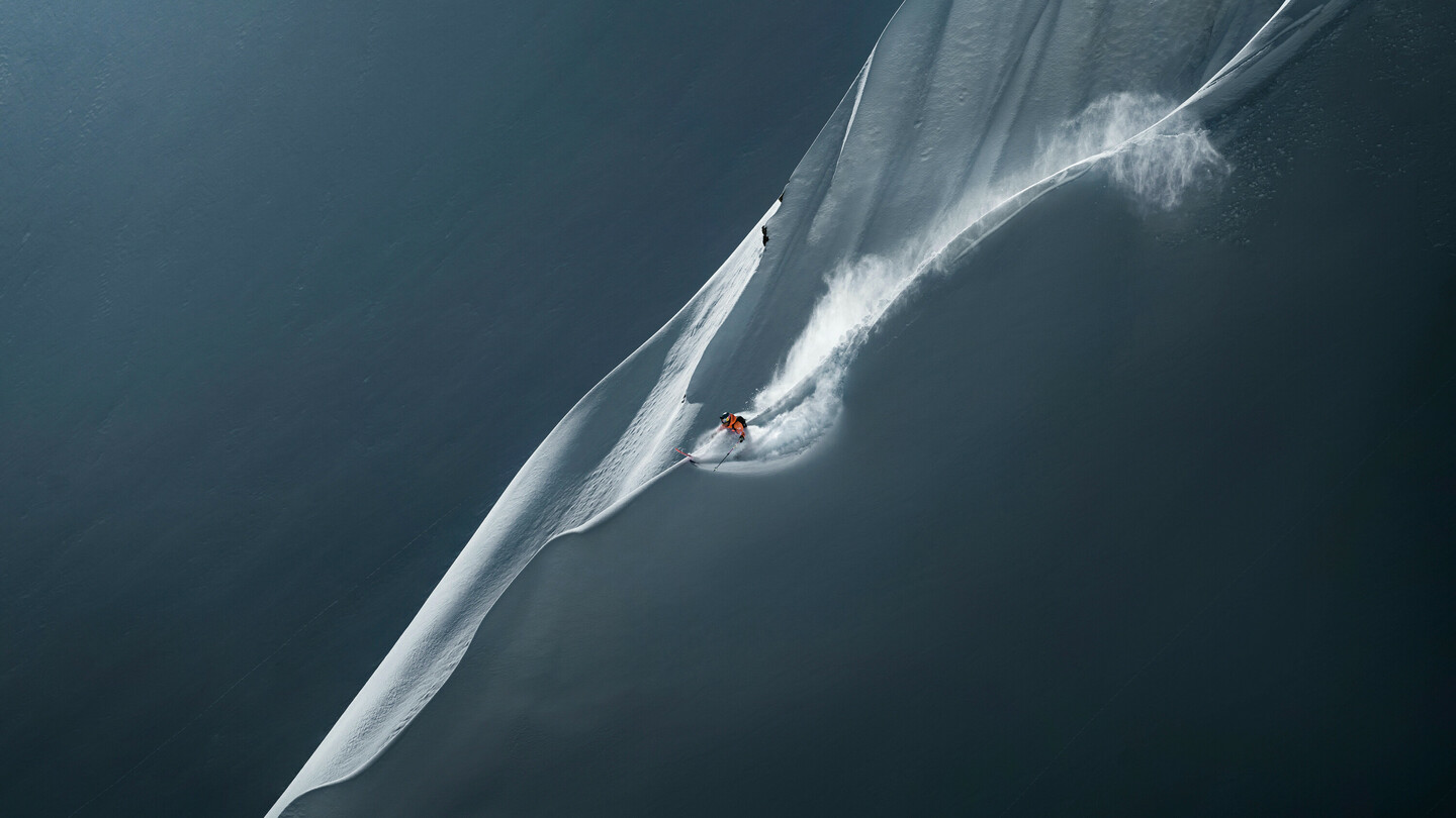 Skier descending a steep, untouched snowy slope, leaving a dynamic trail in the fresh powder snow.